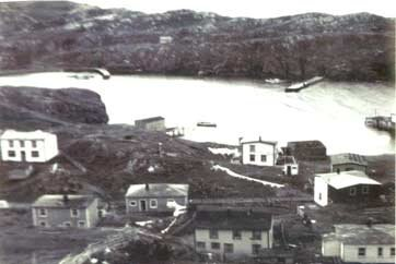 53 Little Merasheen harbour. Houses belonging to (center left) Johnny and Lizzy Ennis with his stage and wharf towards the harbour, bottom left is George and Cicely Wilson, next is Anthony and Theresa Wilson, next is Kate Wilson, right left corner was owned by Ag Pearson and then by Bill and Helen Wilson. In front of that is Johnny and Stella Wilson and the next white house is Hennesseys.&amp;nbsp; Across the harbour is the Priest's Wharf on the left, Jimmy Barrett's house on the hill and then the breakwater.&amp;nbsp; Far right is pat of George Wilsons stage and wharf.